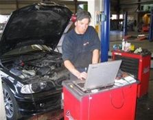 Mann driver med automatservice og jobber på bil med laptop med bil i bakgrunnen