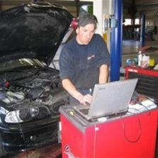 Mann driver med automatservice og jobber på bil med laptop med bil i bakgrunnen